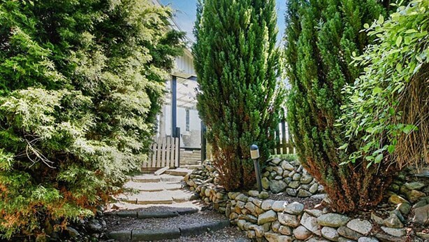Un sendero de piedra que conduce a una puerta de madera, rodeado de árboles de hoja perenne.
