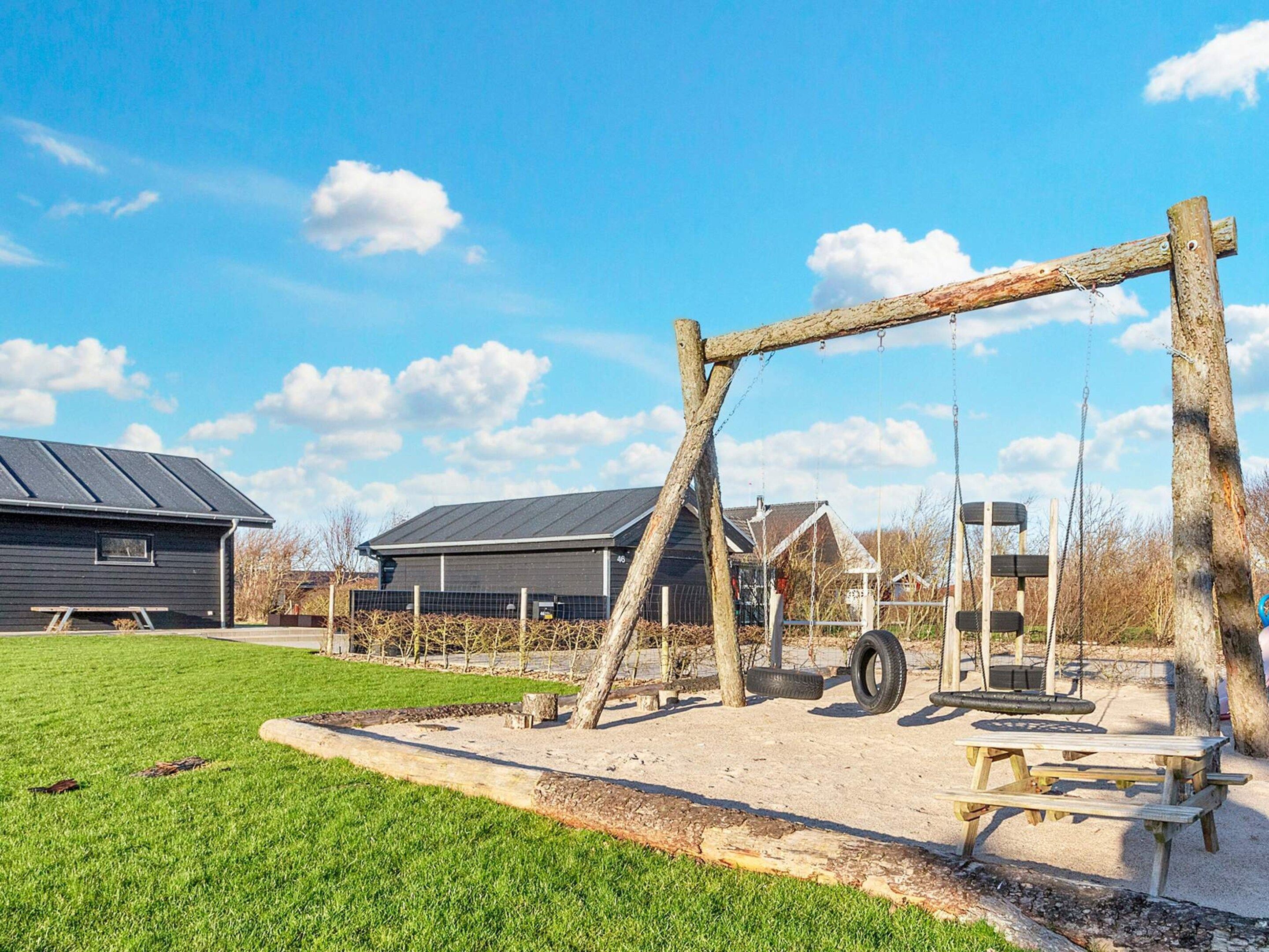 A playground with a swing set, picnic table, and a building with a dark roof.