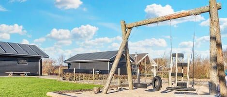 A playground with a swing set, picnic table, and a building with a dark roof.