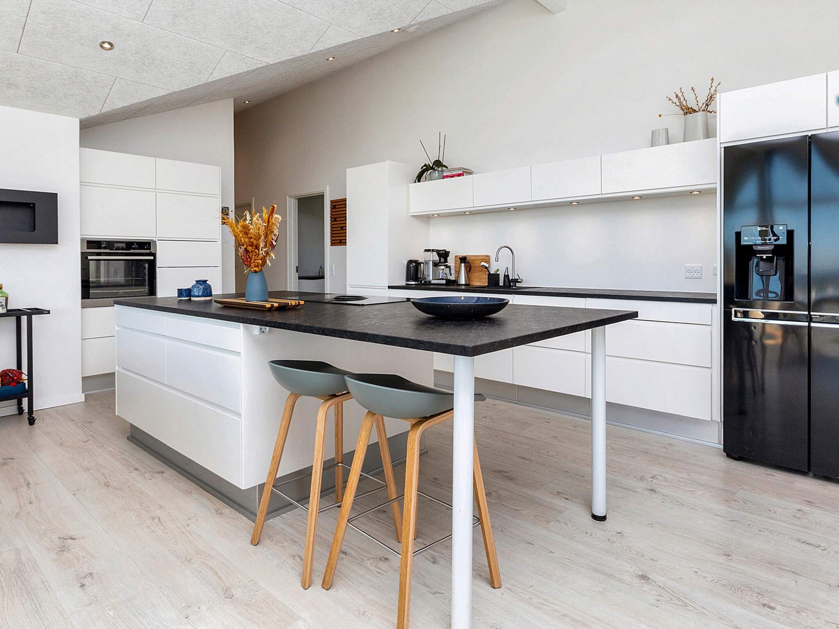 Et moderne køkken med en central ø, barstole, indbygget ovn og et sort køleskab.