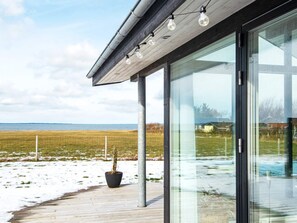 A modern building with large glass windows, a wooden deck, and a view of the sea. - 4 Star Holiday Home in Vinderup (Vinderup)