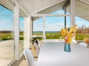 Ein moderner Essbereich mit einem großen Tisch, weißen Stühlen und Meerblick durch große Fenster.