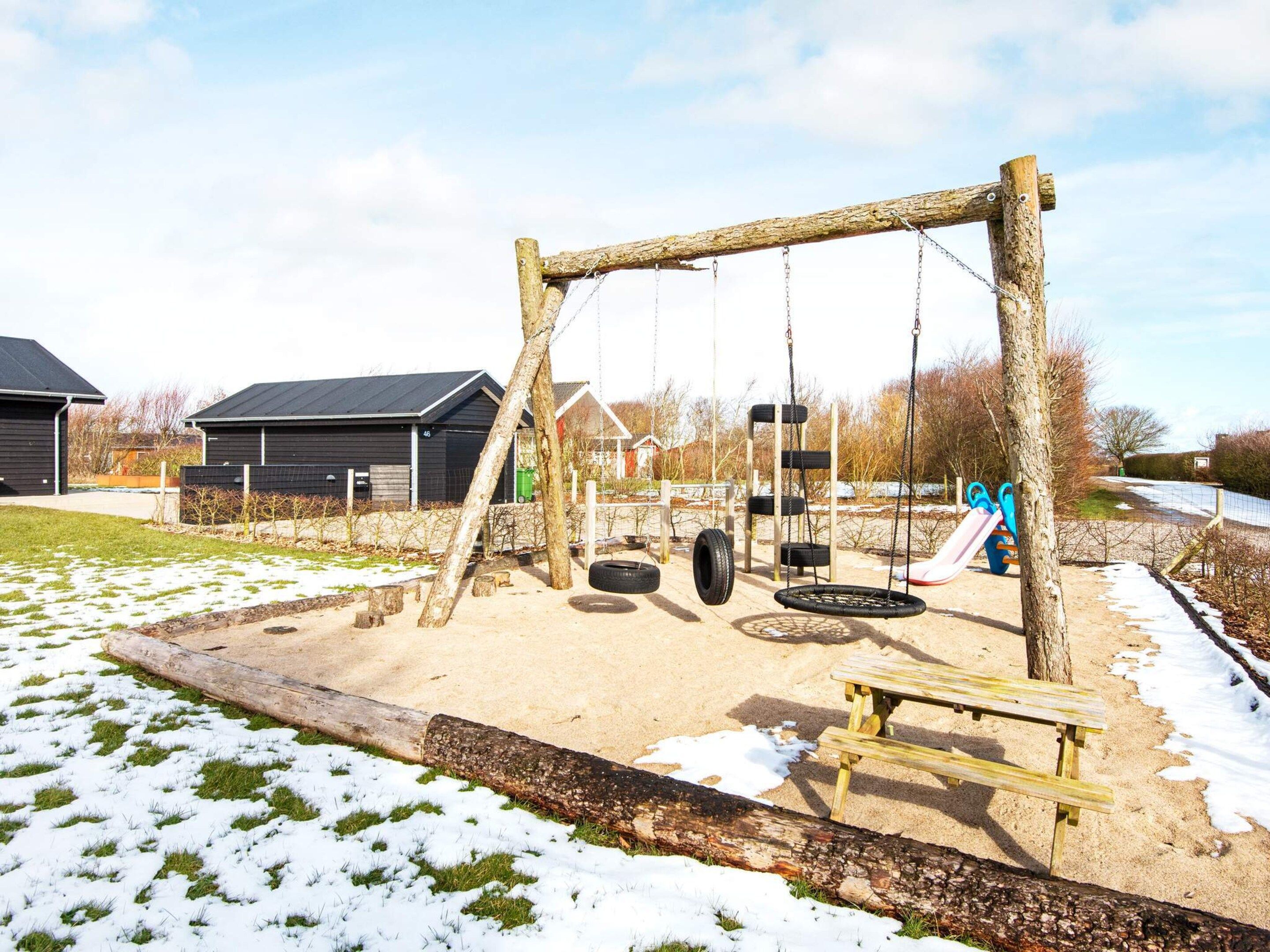Un parque infantil con columpios, un neumático colgante y un tobogán.