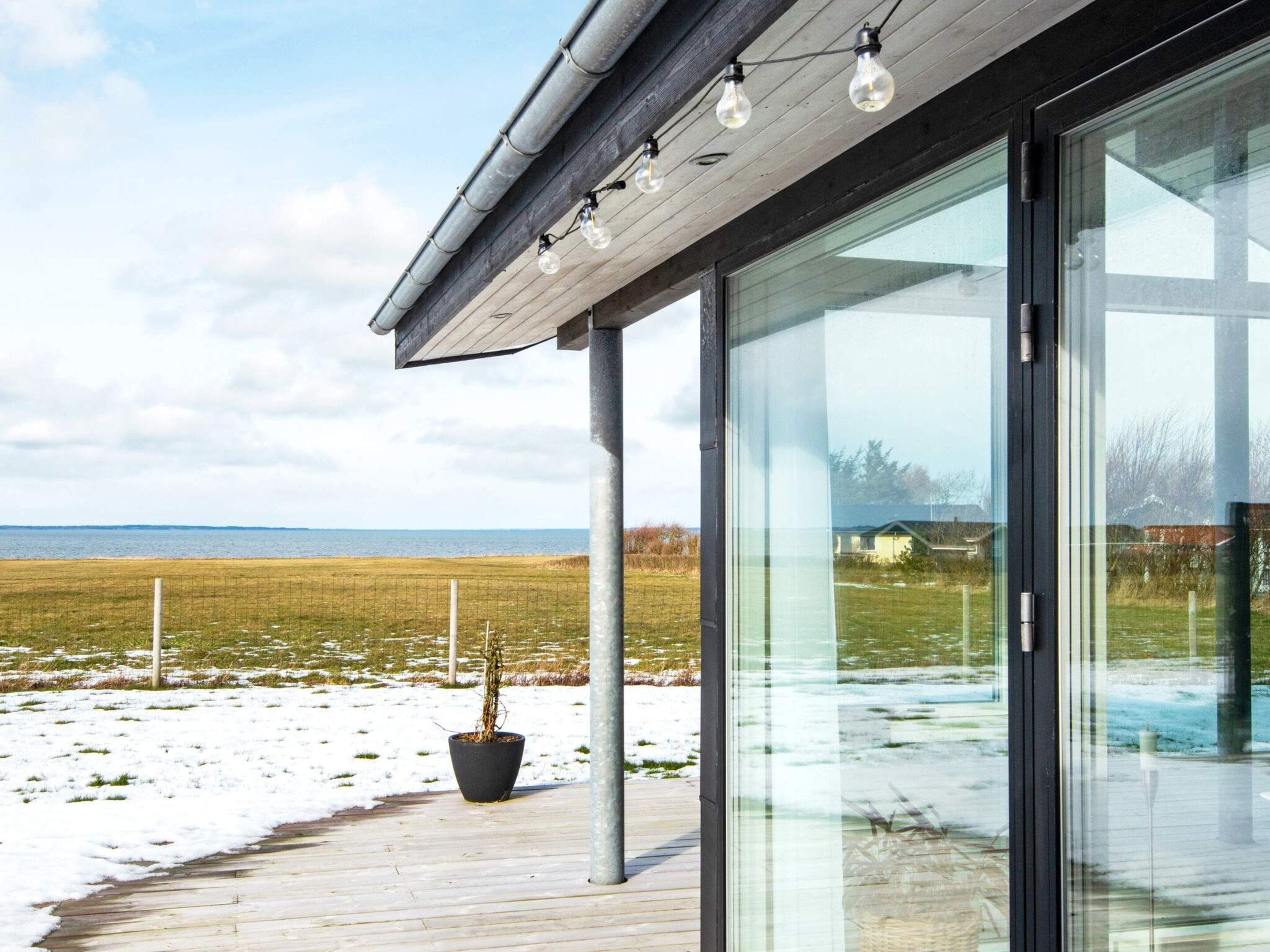 A modern building with large glass windows, a wooden deck, and a view of the sea.