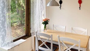 A dining area with a wooden table, white chairs, a vase with flowers, and a window with lace curtains. - 5 Person Holiday Home in Vaddo (Väddö)