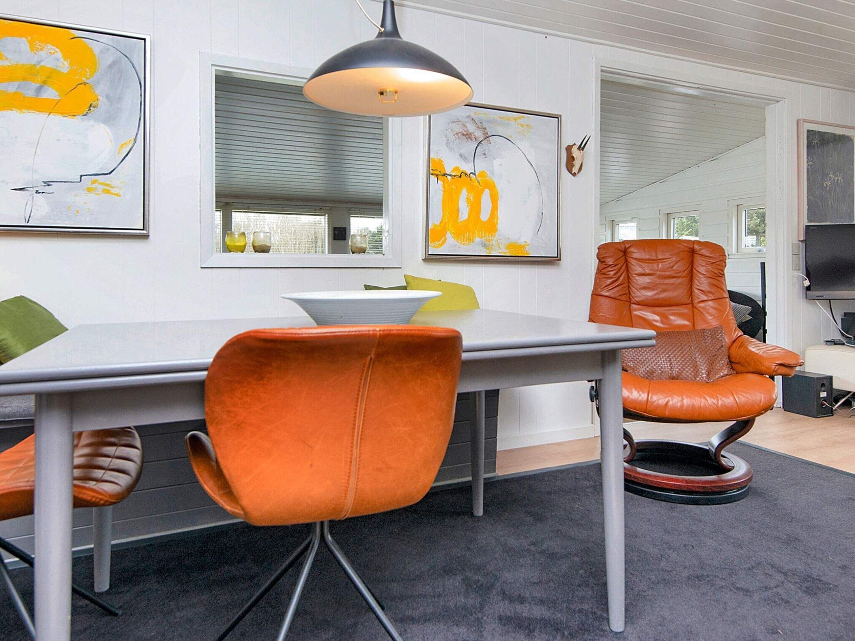 A modern dining area with a white table, orange chairs, and a black pendant light.