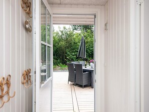 Een open deur die leidt naar een terras buiten, met rieten meubels en een tafel gedekt voor een maaltijd.
