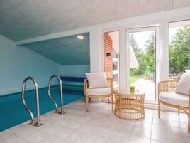 Zona de piscina con puerta de vidrio que da al exterior, mobiliario de mimbre y una pared de acento azul.