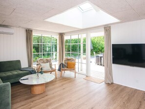 A room with a green sofa, a glass coffee table, two armchairs, a TV, and a large window with a view of greenery. - 8 Person Holiday Home in Henne (Henne)