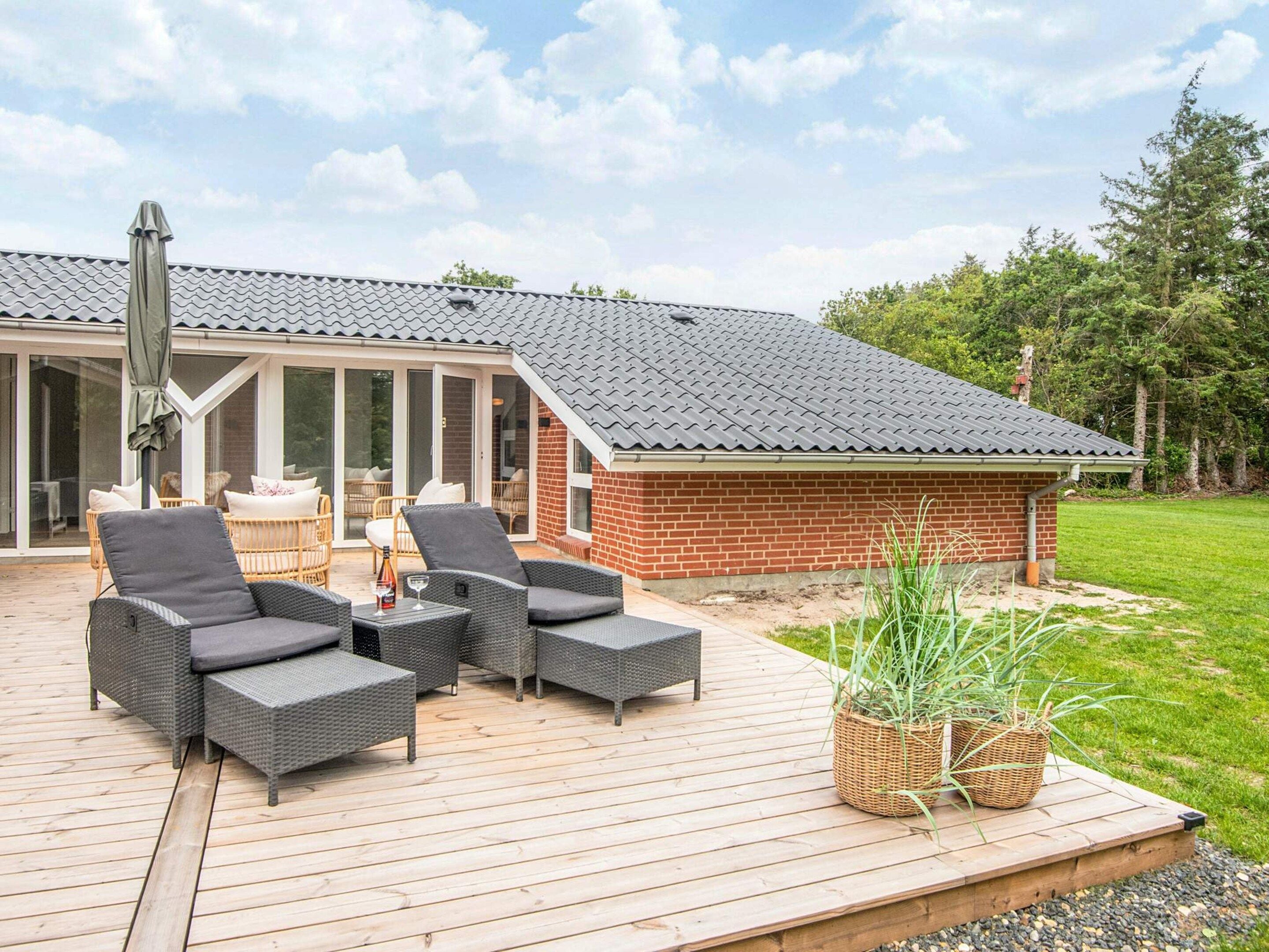 Una terraza techada al aire libre con mobiliario de mimbre, una estructura de ladrillo y un jardín con césped.