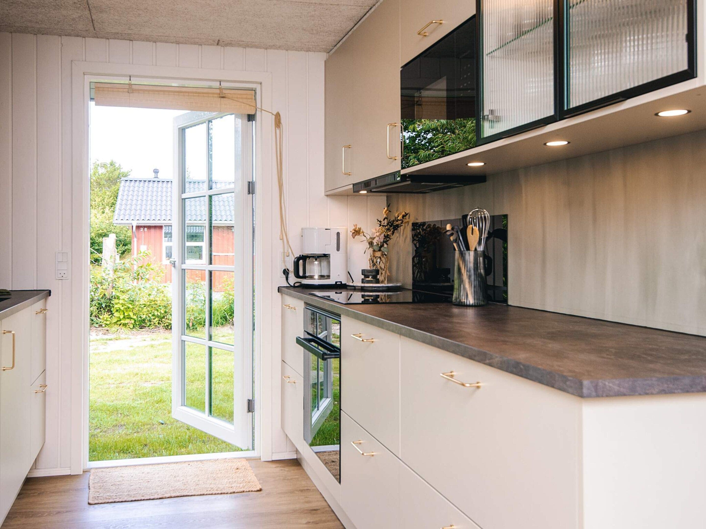 A modern kitchen with a built-in oven, a coffee maker, and a window overlooking a garden.