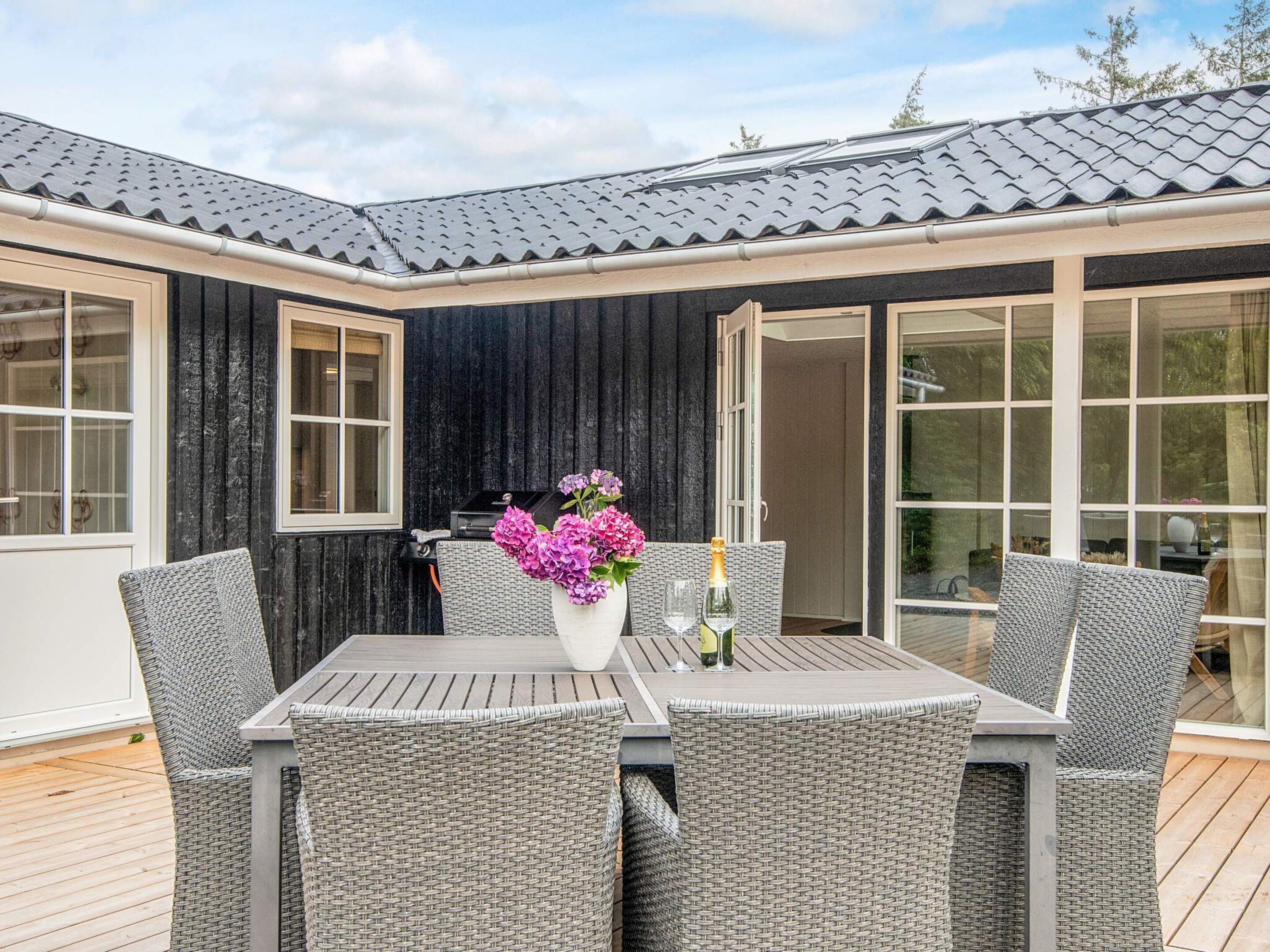 Une terrasse avec une table et quatre chaises en osier, un vase rempli de fleurs et une bouteille de champagne.
