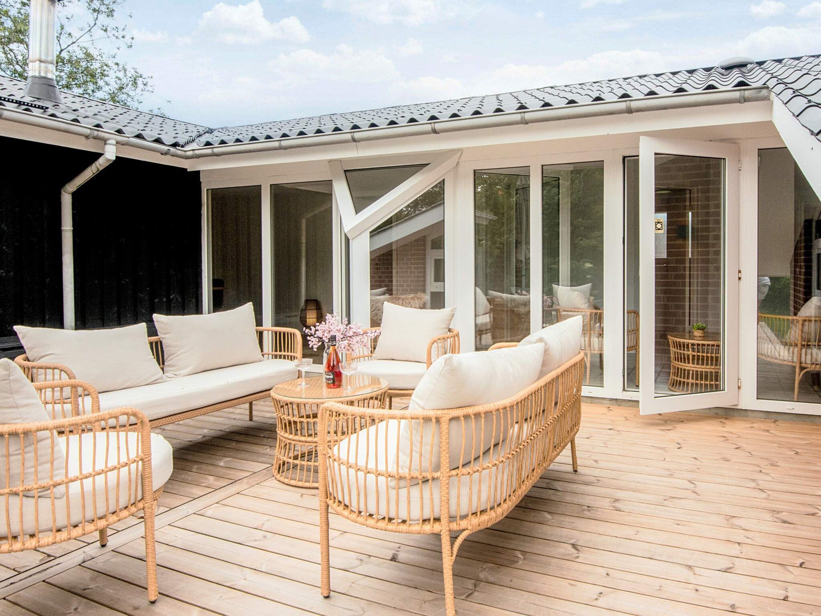A covered outdoor seating area with wicker furniture and a glass door leading to a room.