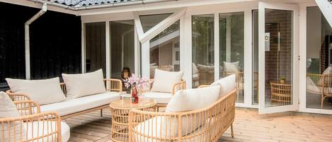 A covered outdoor seating area with wicker furniture and a glass door leading to a room.