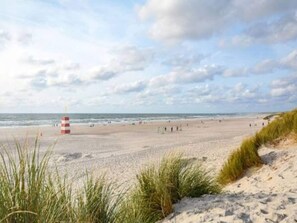 A beach with sand dunes, a red and white striped marker, and the ocean in the background. - 8 Person Holiday Home in Henne (Henne)