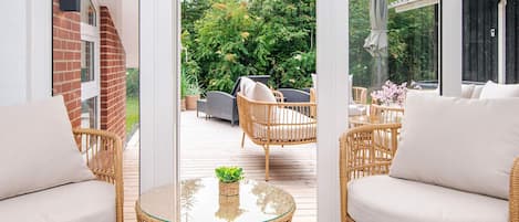 Una habitación con mobiliario de mimbre, una mesa de vidrio y vistas a un jardín.