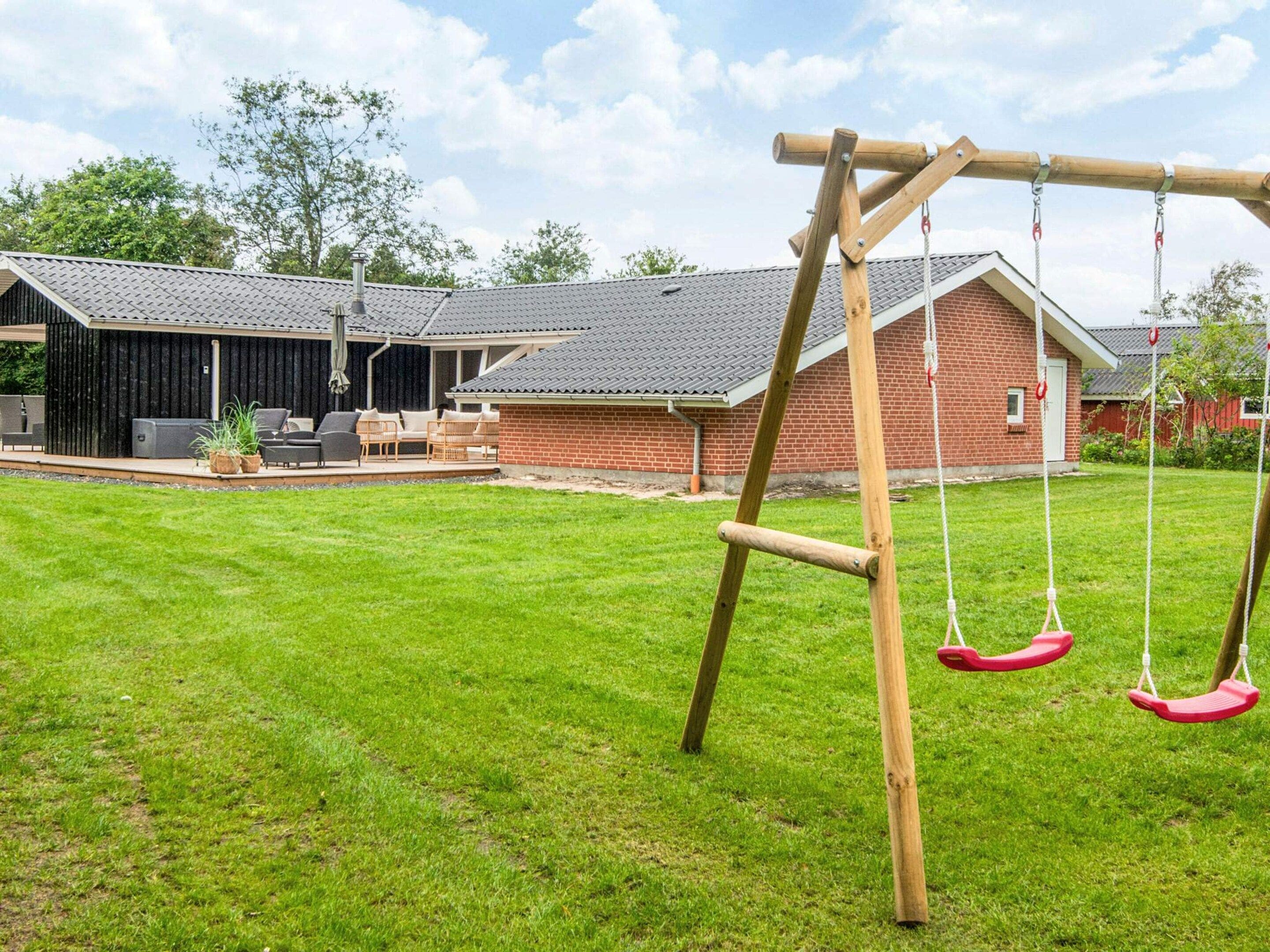 A backyard with a swing set, a covered patio area, and a brick house.