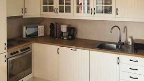 Una cocina con armarios blancos, microondas, cafetera y pileta.