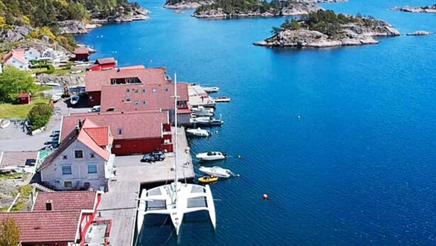 Un pueblo costero con un puerto deportivo, edificios de techos rojos y un mar azul y transparente.