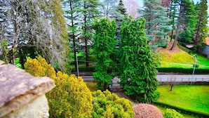 Ein angelegter Garten mit verschiedenen Bäumen und Sträuchern, einem gepflasterten Weg und einem ehrfurchtgebietenden Eingangstor.