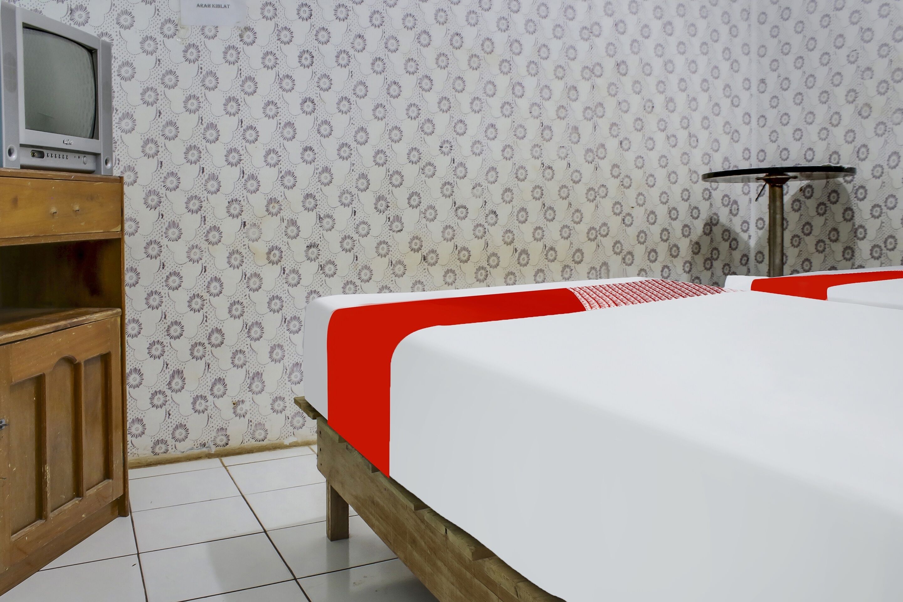 A hotel room with a wooden cabinet, a television, a patterned wallpaper, and a bed with red and white bedding.