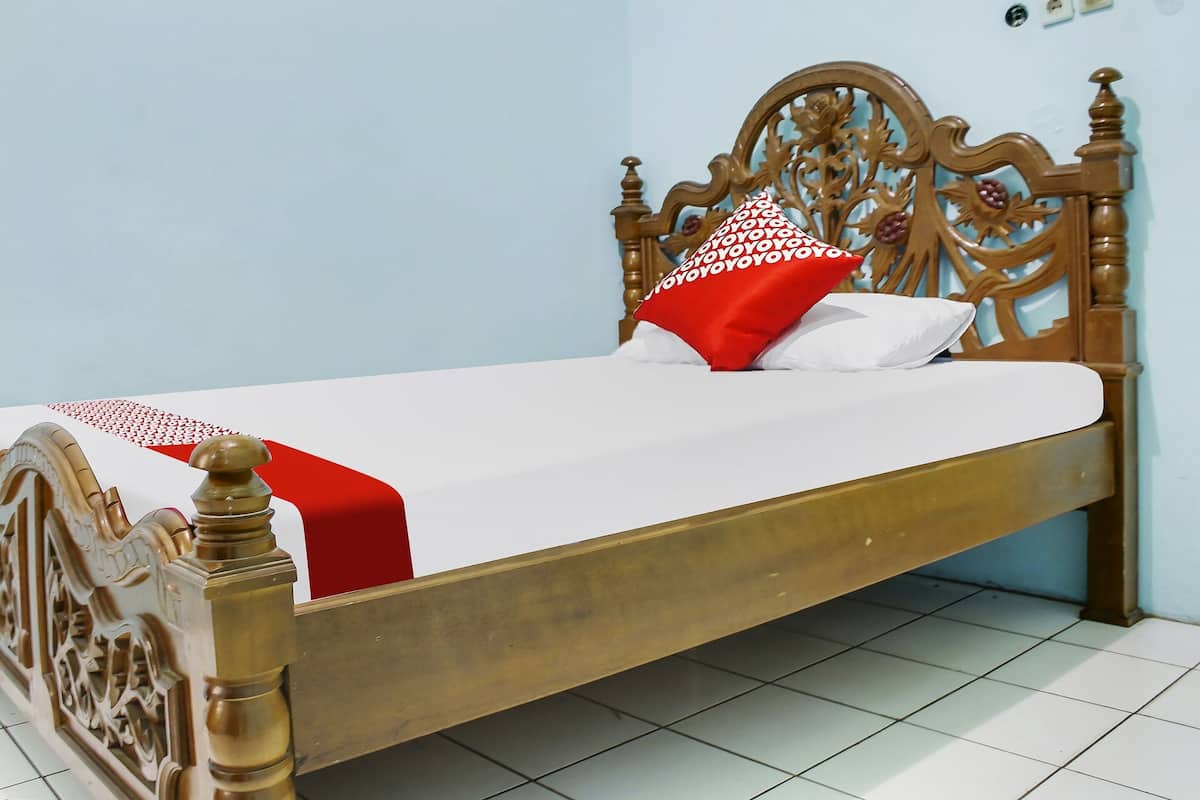 Een keurig opgemaakt bed met een houten hoofdbord, witte beddengoed en een kussen met een rood-wit patroon.