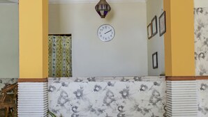 Een kamer met een klok, lijstjes, een hanglamp en behang met bloemenmotief.
