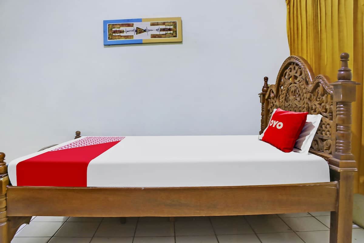 Een net opgemaakt bed met een rode en witte dekbedovertrek, een houten hoofdbord en een enkel rood kussen met de tekst 'POVO'.