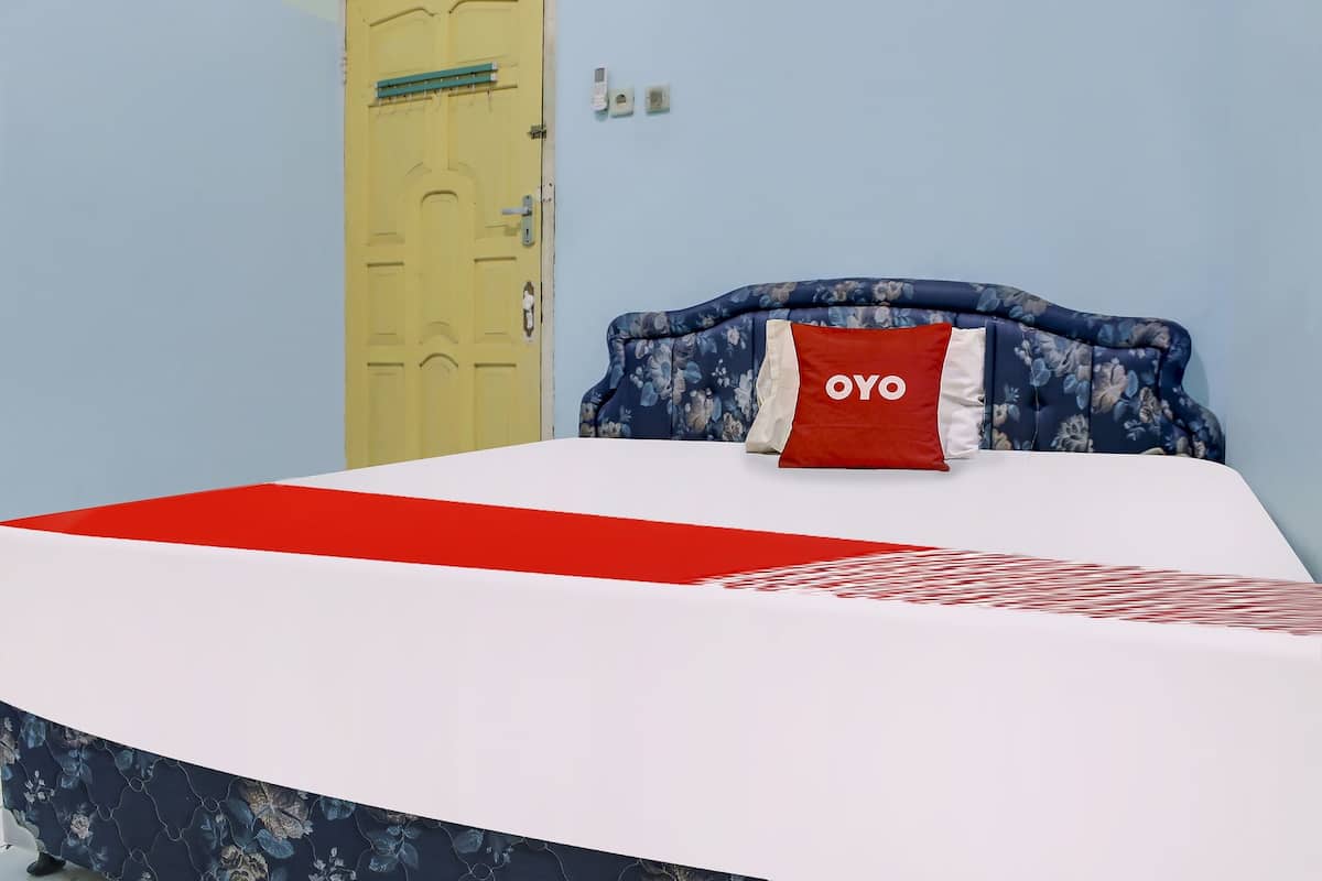Een bed met een hoofdbord met bloemenprint, een rood-wit kussen en een rood-witte dekbedovertrek.