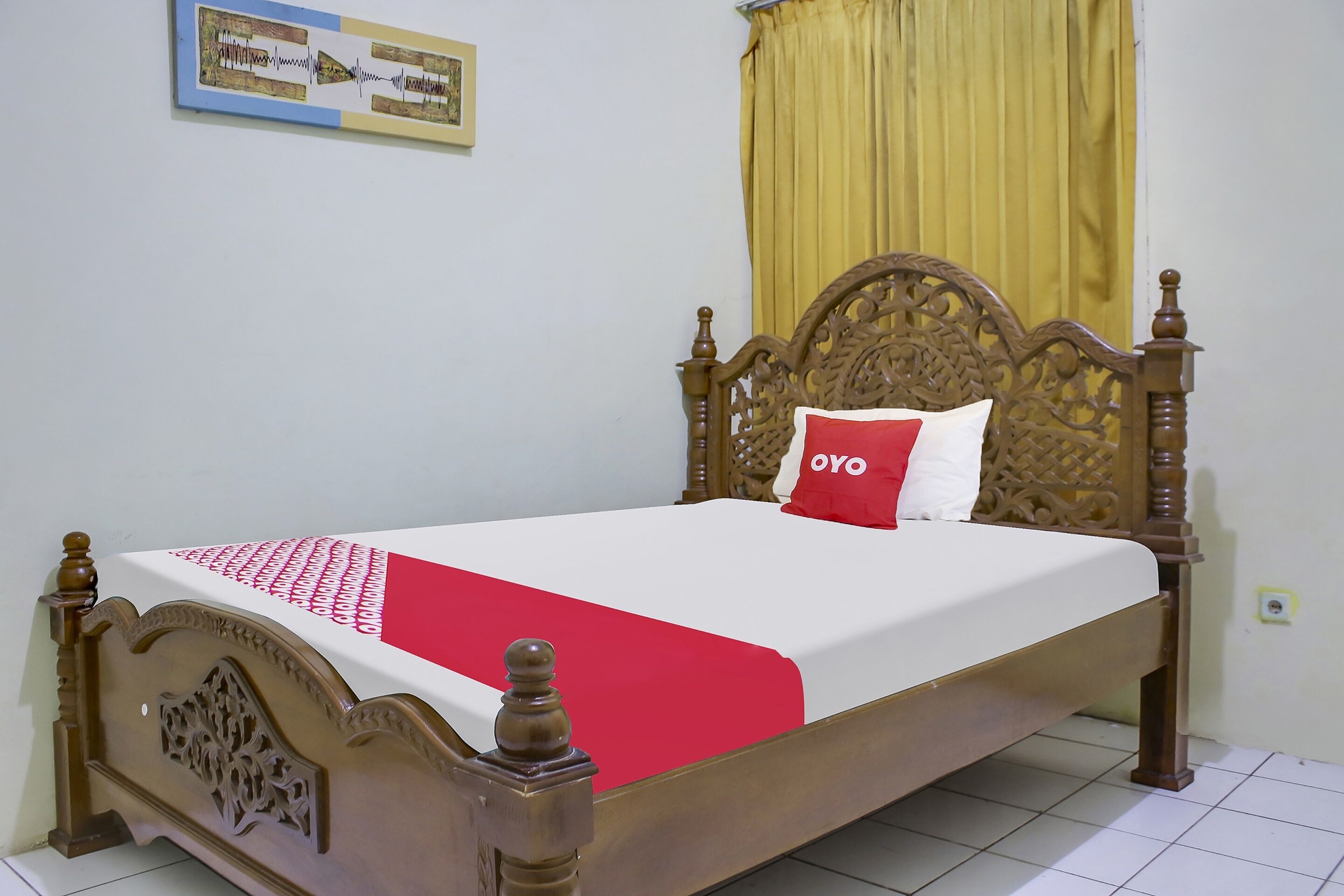 Een houten bed met een rood-witte dekbedovertrek, een rood kussen en een geel gordijn.