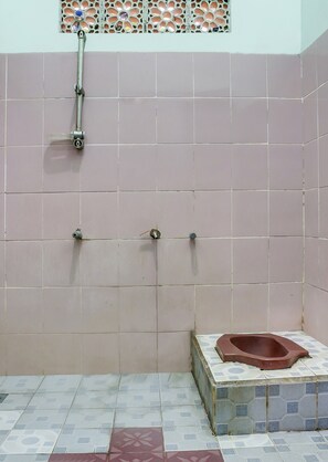 Shower area with a metal hose and single showerhead, set against a backdrop of patterned tiles.
