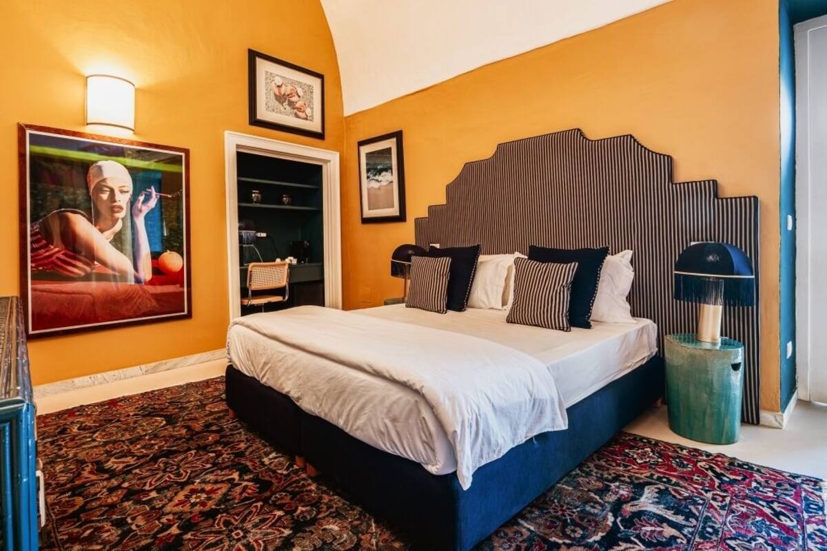 A bedroom with a large bed, a headboard with vertical stripes, a patterned rug, and a framed picture on the wall.