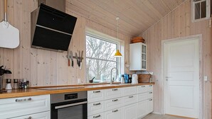 A kitchen with wooden walls, white cabinets, a built-in oven, and a window with a view of trees. - 5 Person Holiday Home (Vordingborg)