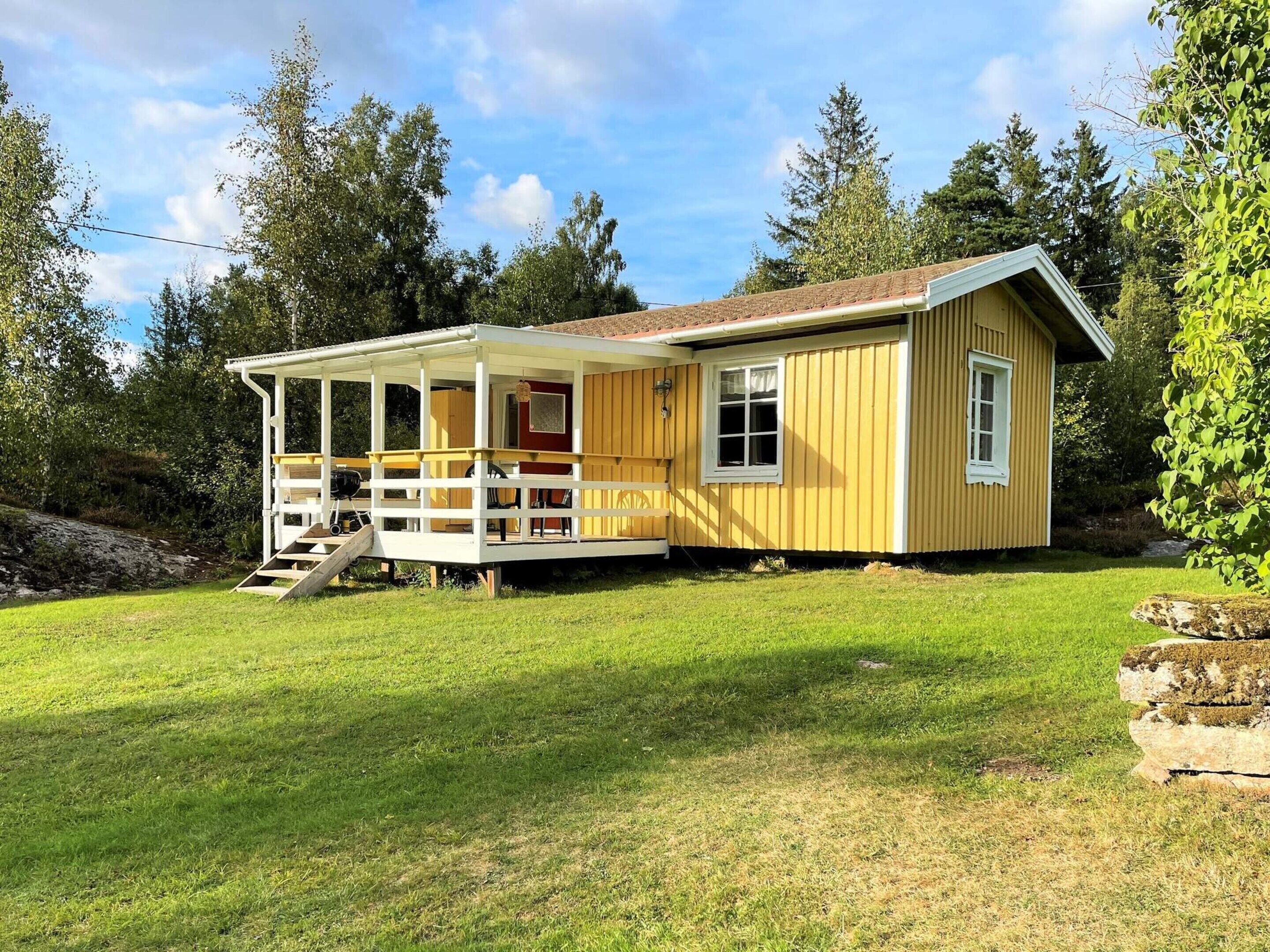 A yellow cabin with a covered porch and a small deck, surrounded by a grassy yard and trees.