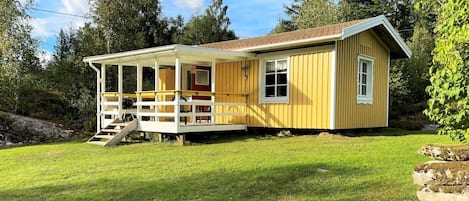A single-story yellow cabin with a porch, a small deck, and a stone structure in the foreground.