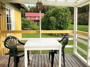 A covered outdoor seating area with a table and chairs, overlooking a well-maintained lawn and a red house in the background. - 2 Person Holiday Home in Henan (Henån)