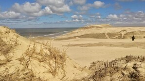 Un paysage côtier avec des dunes, un phare et une personne debout sur le sable.