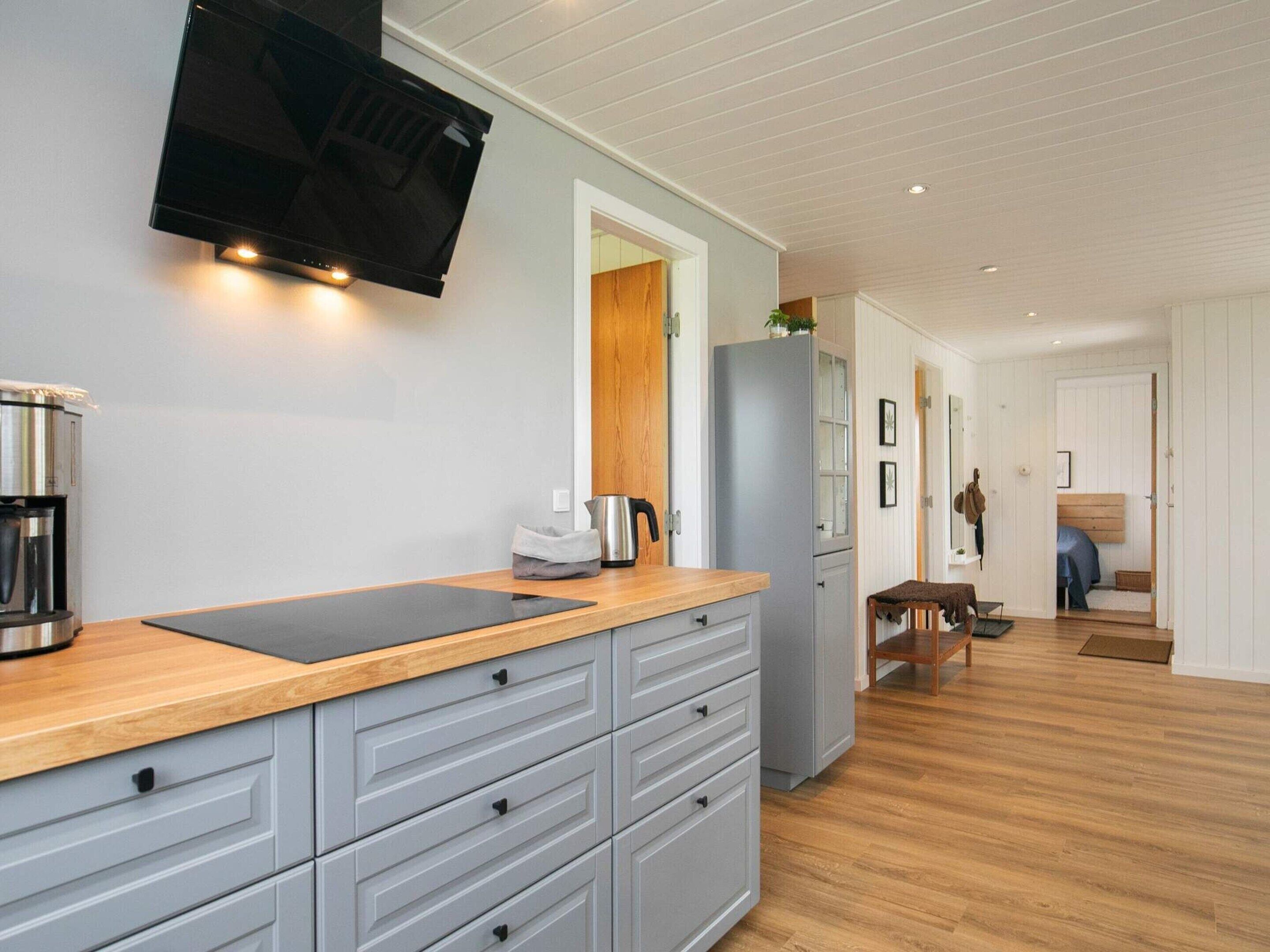 Een moderne keuken met grijze kastjes, een houten aanrechtblad, een ingebouwde kookplaat en een flatscreen televisie boven de kookplaat.