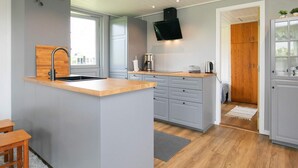 Une cuisine moderne dotée d’un îlot central, de meubles de rangement gris, de plans de travail en bois, d’un évier encastré et d’un téléviseur à écran plat fixé au-dessus de l’îlot.