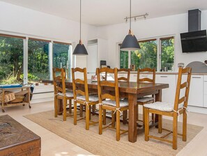 Comedor con mesa y sillas de madera, ventanas amplias y vista a zonas verdes.