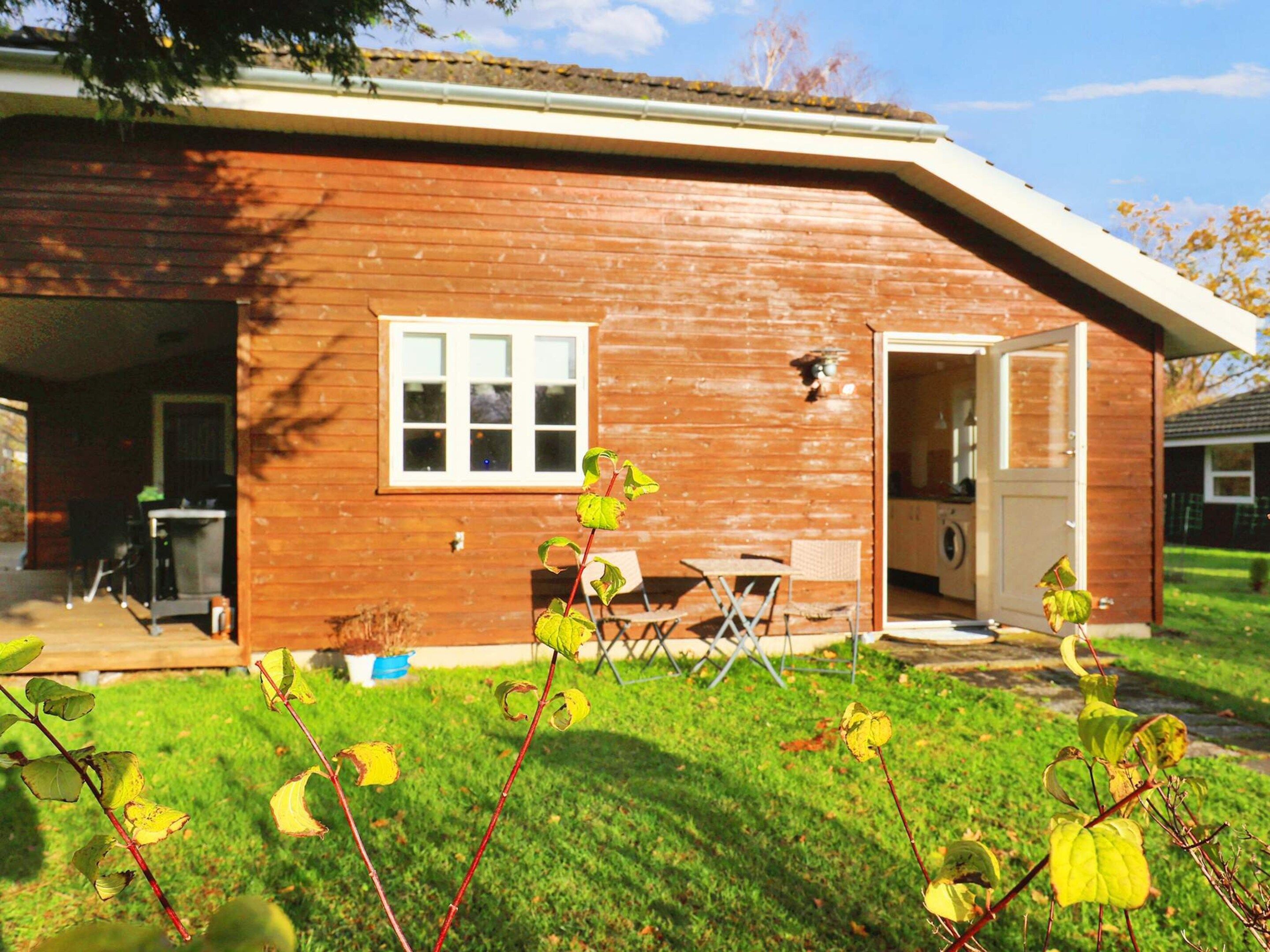 A wooden house with a garage, a small patio with a table and chairs, and a lawn.