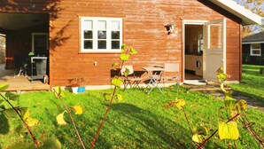 A wooden house with a garage, a small patio with a table and chairs, and a lawn. - 6 Person Holiday Home in Nysted (Nysted)