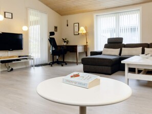 A modern living room with a flat-screen TV, a sofa, a desk, and a round table with a book. - 6 Person Holiday Home in Nysted (Nysted)