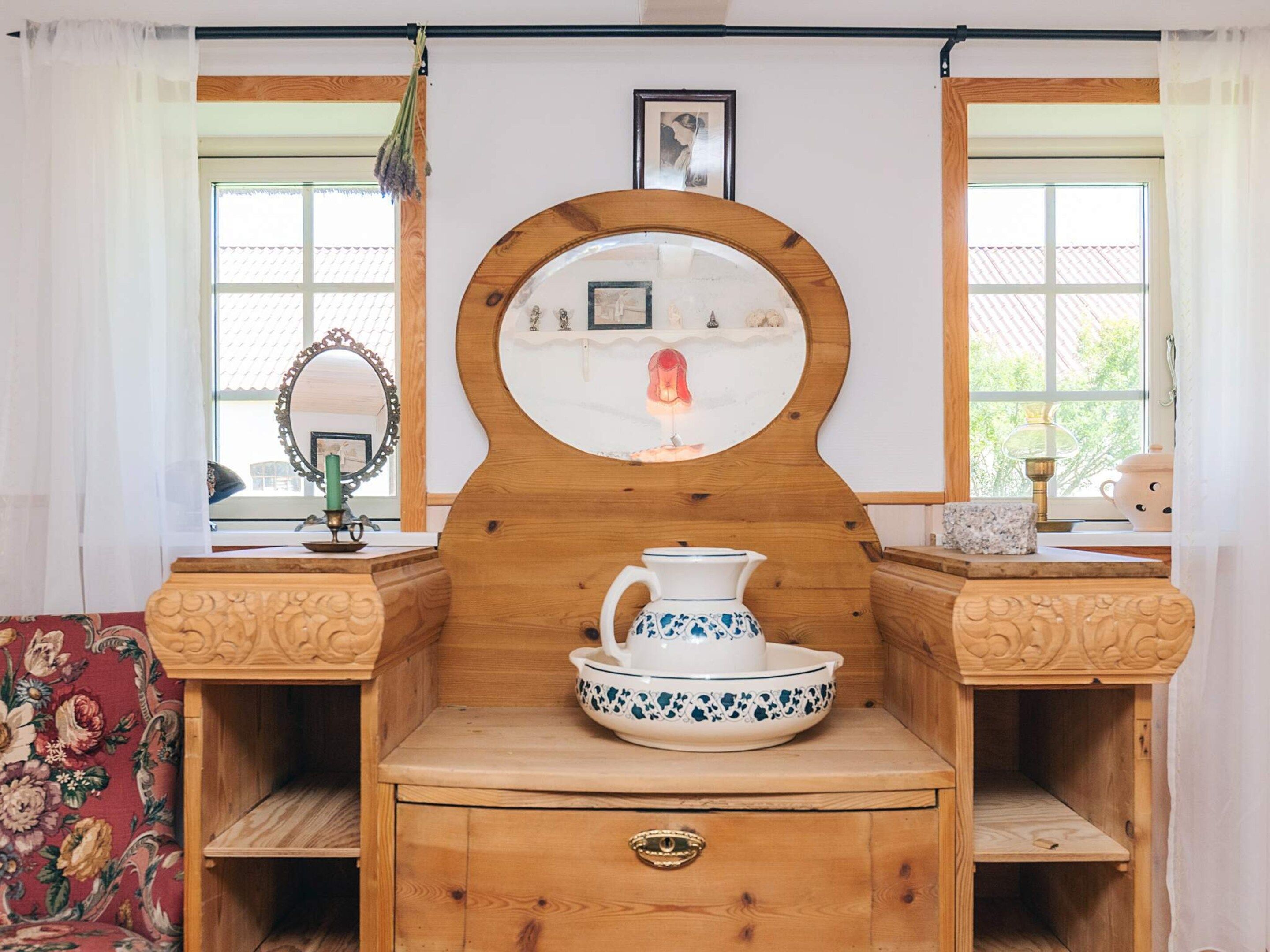 A wooden vanity with a mirror, a pitcher, and a bowl.