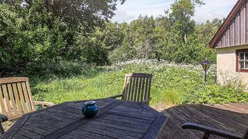 An outdoor seating area with a wooden table and chairs, surrounded by lush greenery and a stone wall.