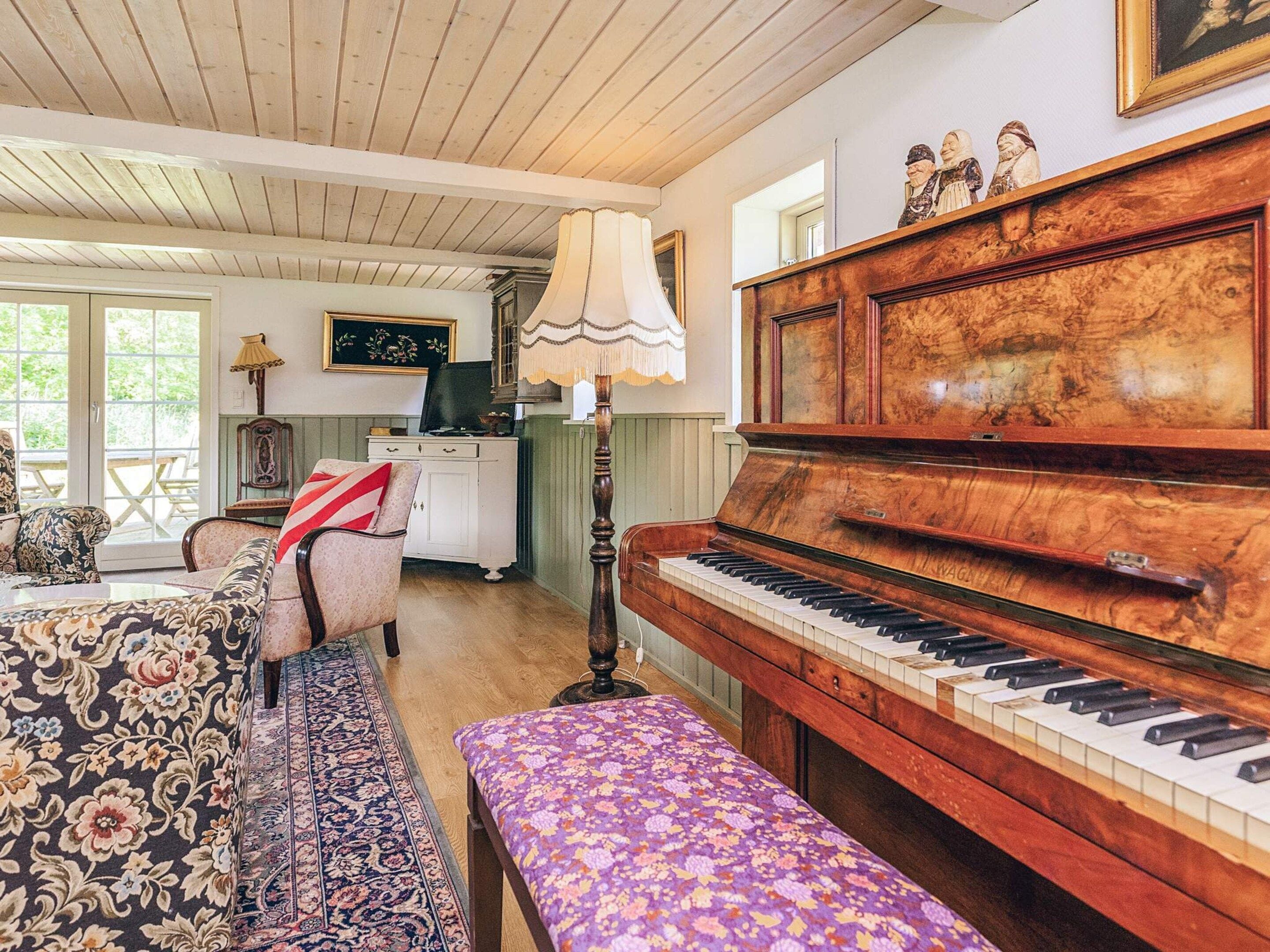 A cozy living room with a grand piano, a patterned sofa, and a bench.