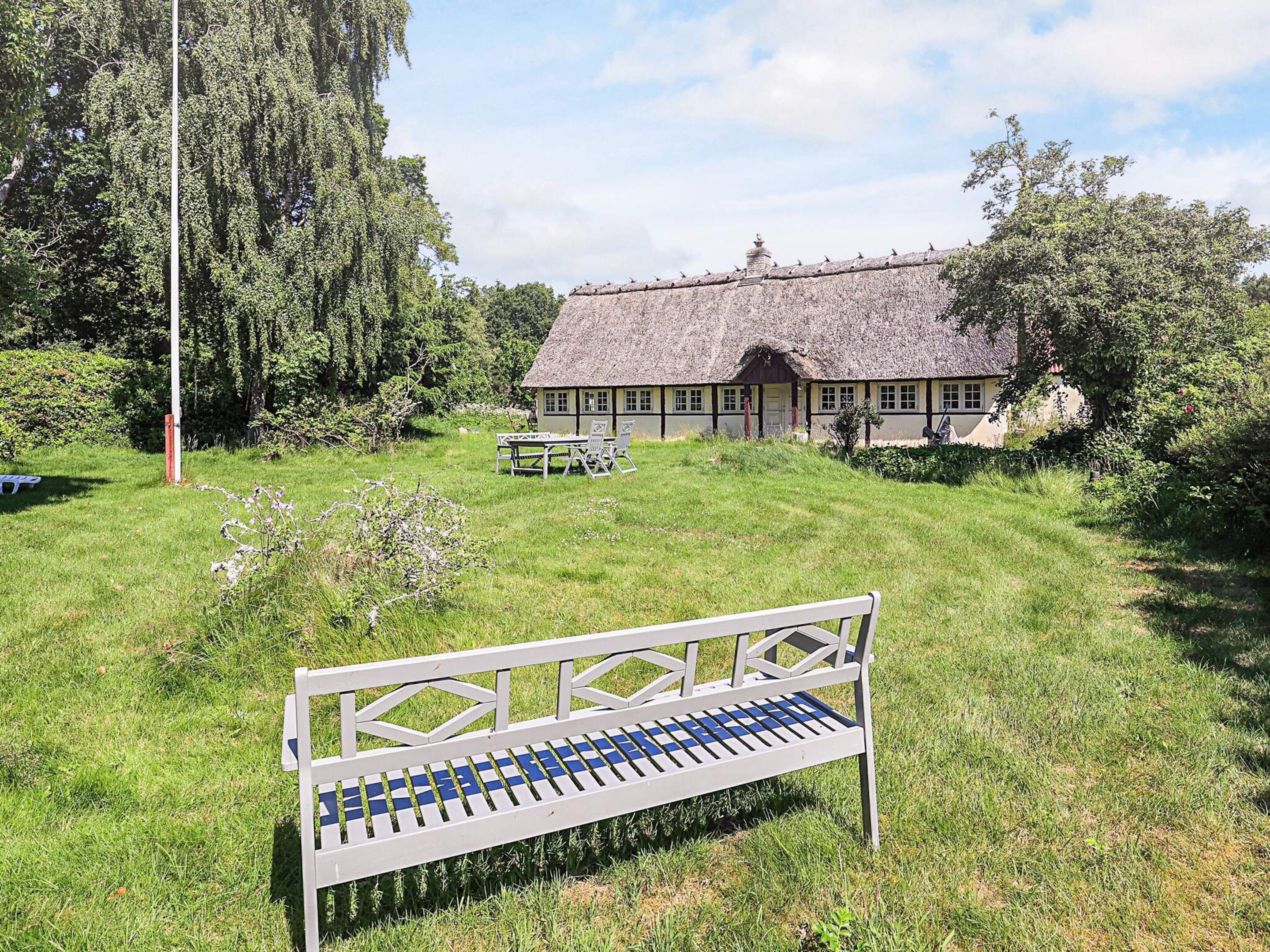 A grassy area with a bench, a thatched-roof building, and trees.
