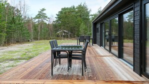 A modern outdoor deck with a dining table and chairs, surrounded by a natural forest setting. - 8 Person Holiday Home in Laeso (Læsø)