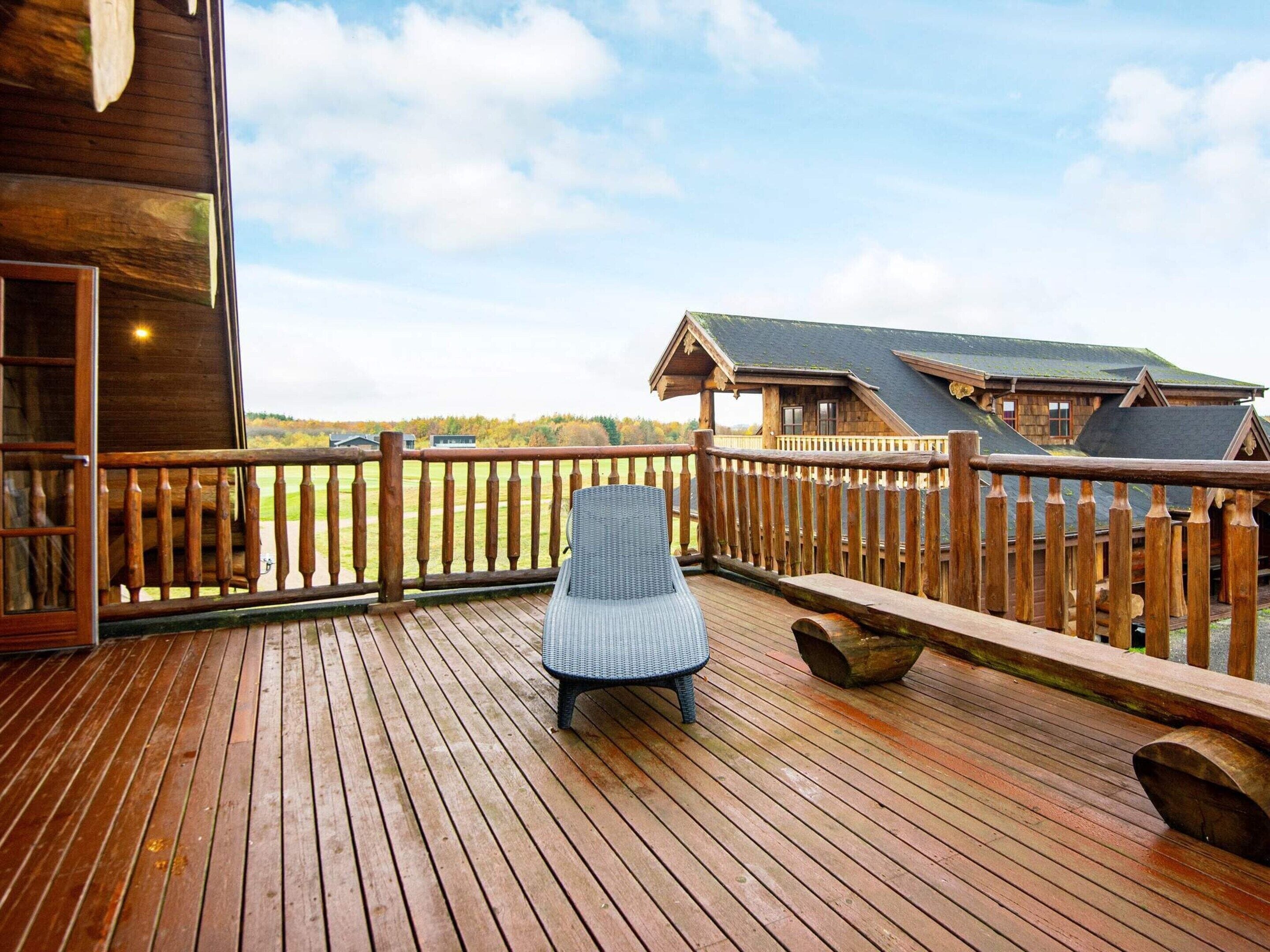 A wooden deck with a wicker chair, wooden railings, and a view of a building and landscape.