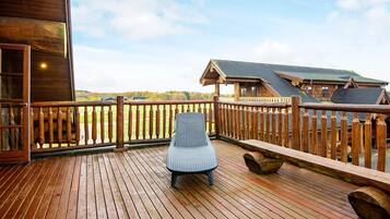 A wooden deck with a wicker chair, wooden railings, and a view of a building and landscape.